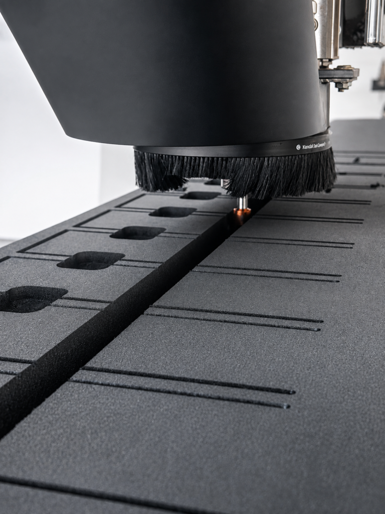 Close-up of a CNC machine cutting head with a bristle brush over a perforated worktable bed.