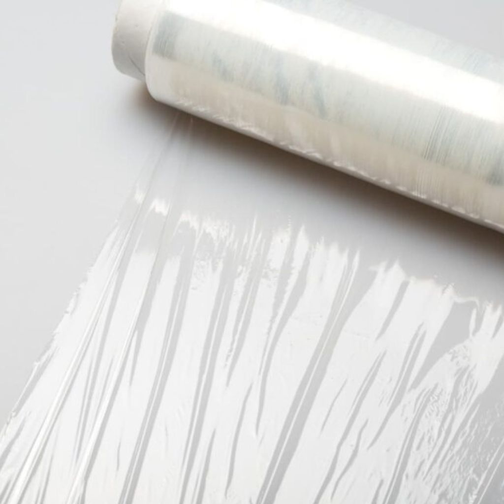 Roll of transparent plastic wrap with a sheet partially unrolled on a white surface around the top edge of the image.