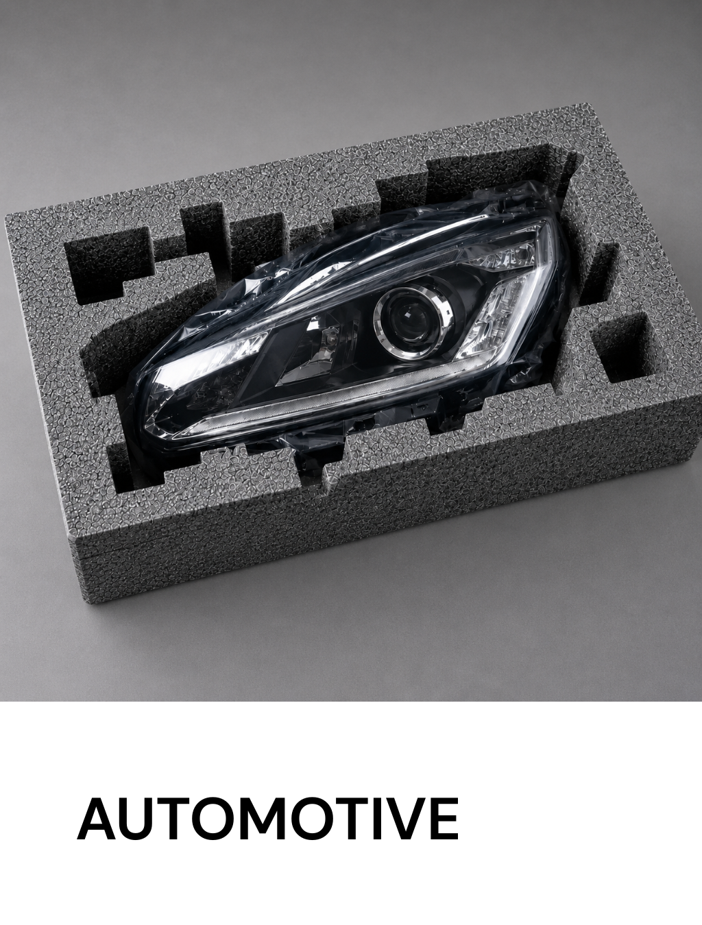 Automotive headlight packaged in a foam insert, resting on a gray background with 'AUTOMOTIVE' text below.