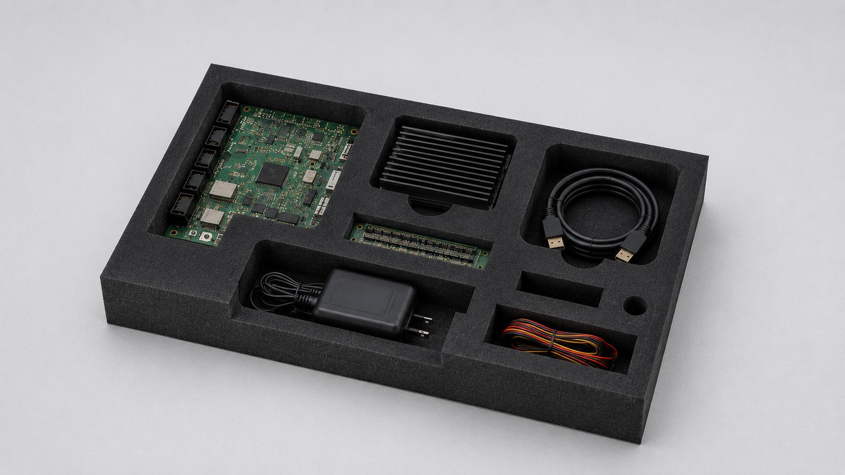 Foam tray with a development kit: green PCB, large heatsink, PCIe edge connector, power adapter, USB cable, and bundled wires/cords.