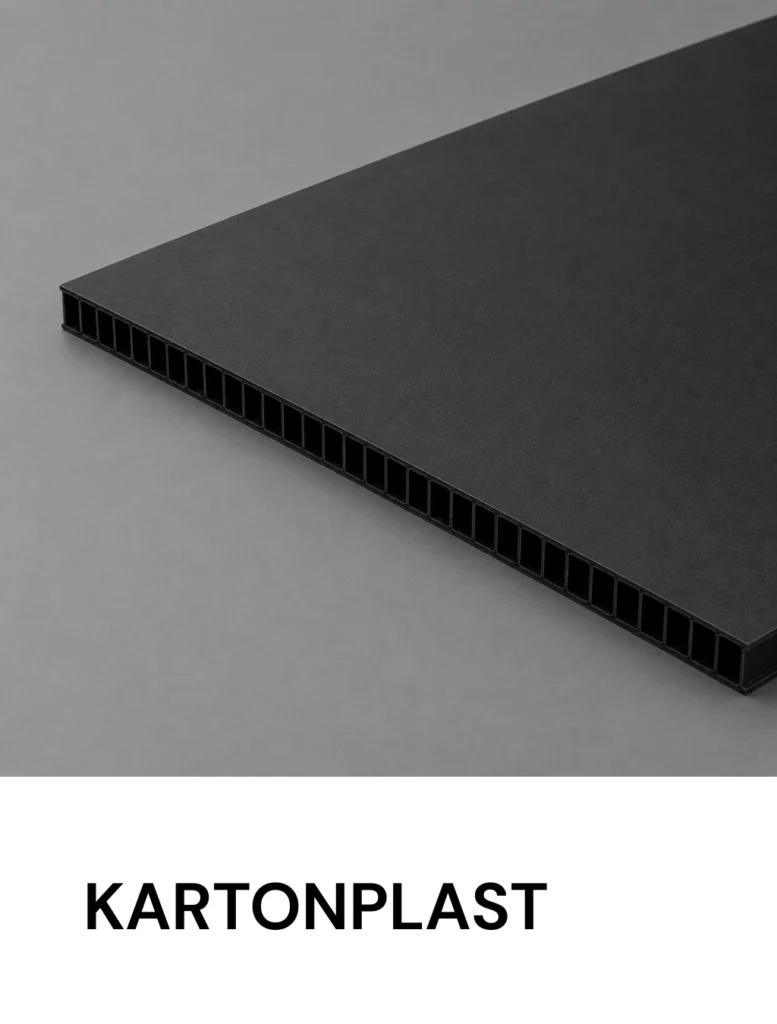 Gray close-up of a black Kartonplast sheet showing its hollow honeycomb-core edge and smooth top surface (brand name visible at bottom).