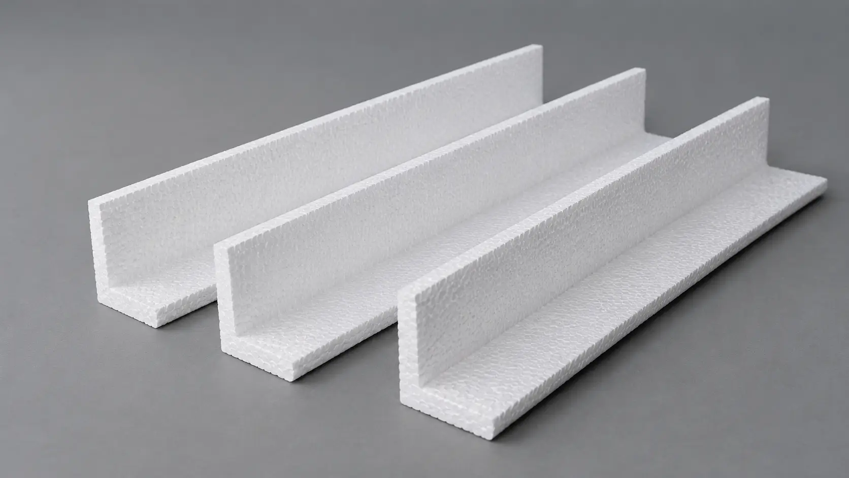 Three white foam U-channel profiles (edge trims) arranged on a gray surface, likely polystyrene foam edge protectors used in packaging or insulation.