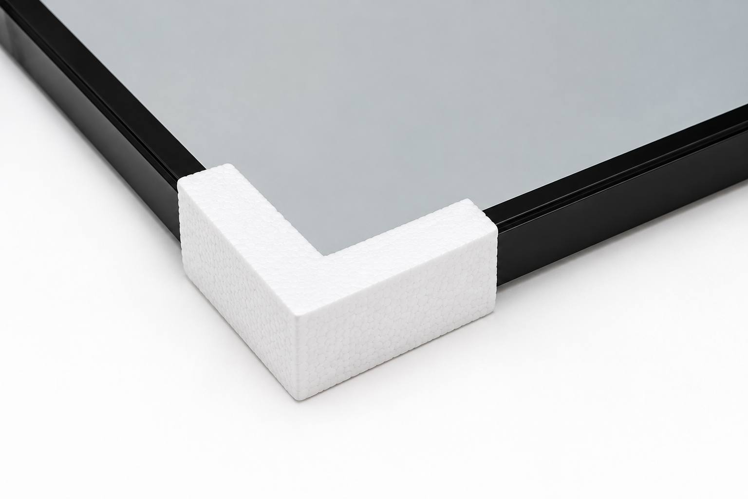 White foam corner protector placed at the edge of a glass panel with a black frame, on a light surface.